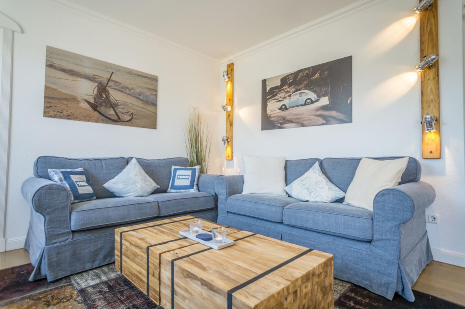Zwei blaue Sofas mit Kissen stehen um einen Holztisch herum. An den Wänden hängen Bilder.