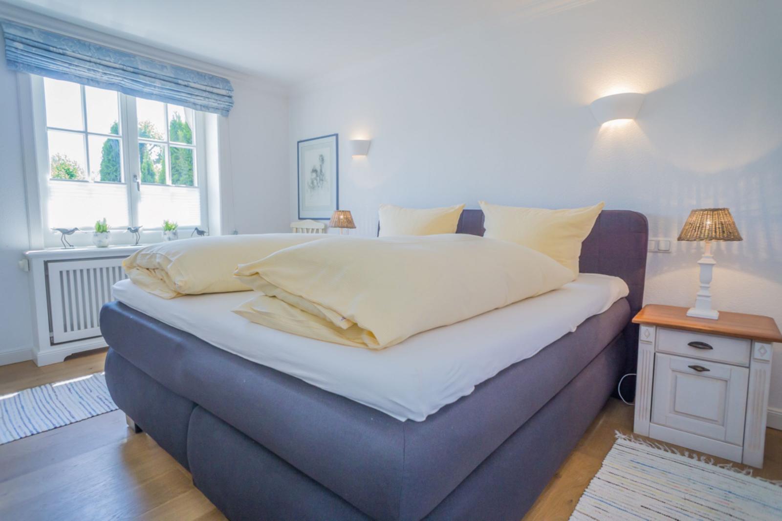 Schlafzimmer mit Bett, Nachttisch und Fenster. Decke und Kissen sind gelb.