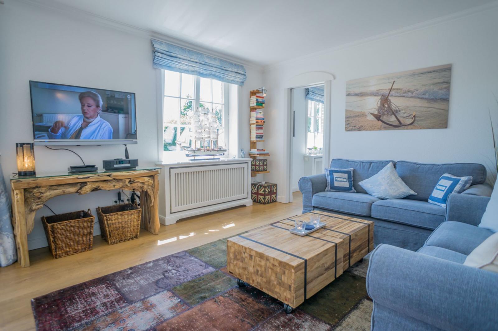 Ein Wohnzimmer mit Sofa, Fernseher und Holztisch. An der Wand hängt ein Bild mit Anker.