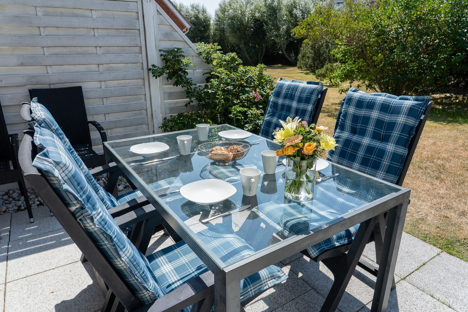 Glas-Tisch mit blauen Kissen und Blumen auf Terrasse