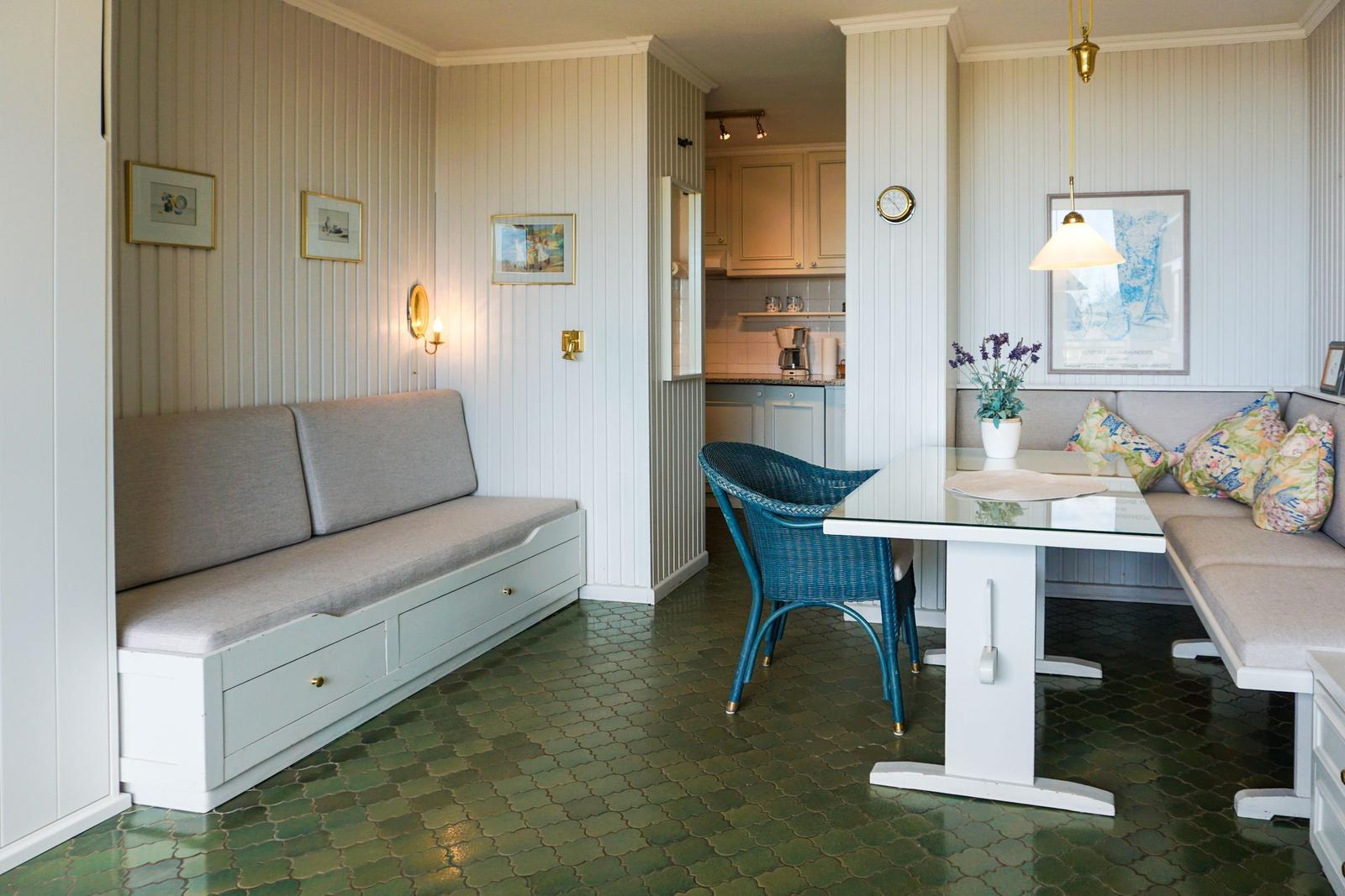 Dining area with table, chair, and sofa. Green tiled floor and white walls.