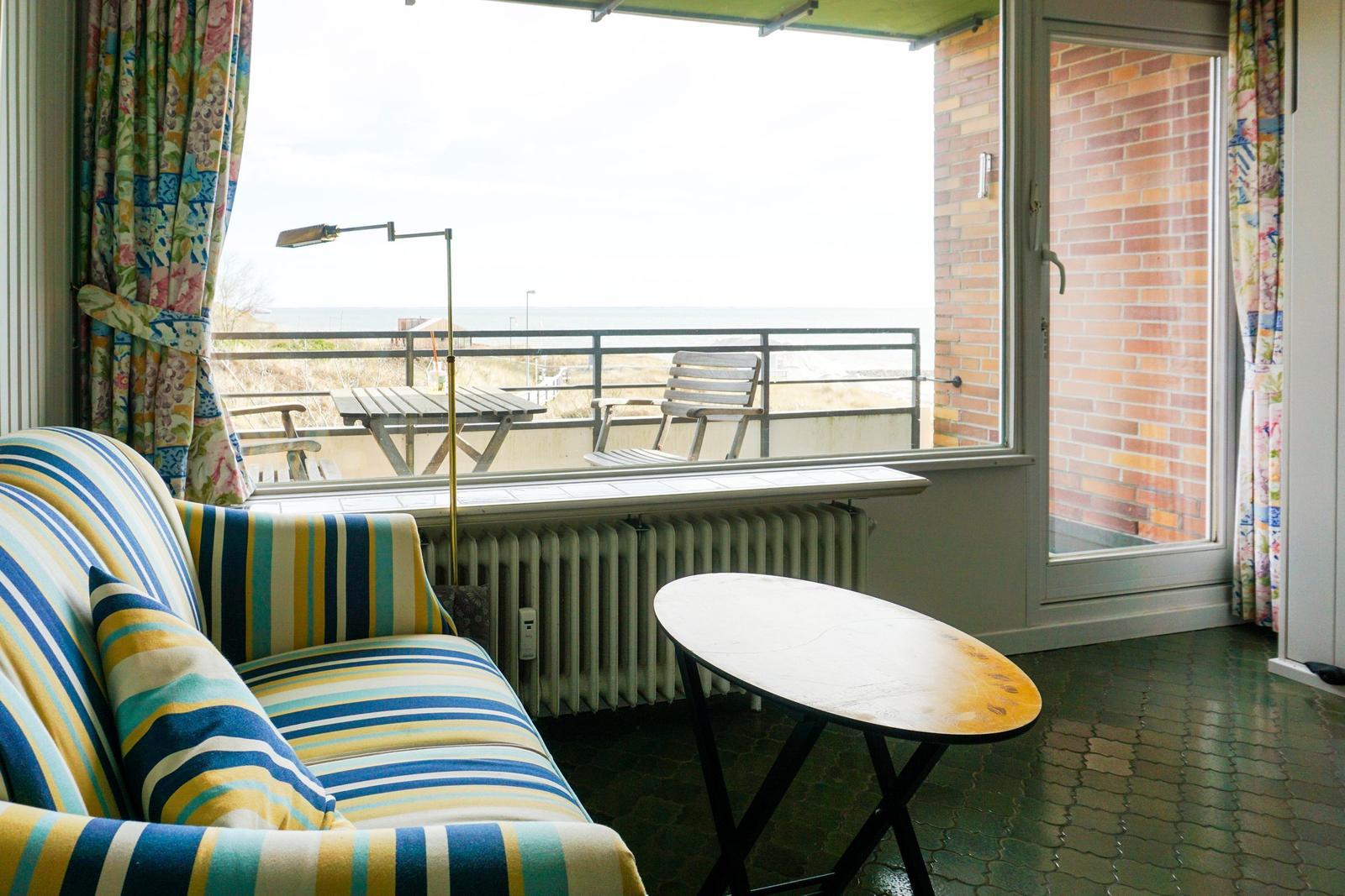 Sofa and table in front of window with view of balcony and sea.