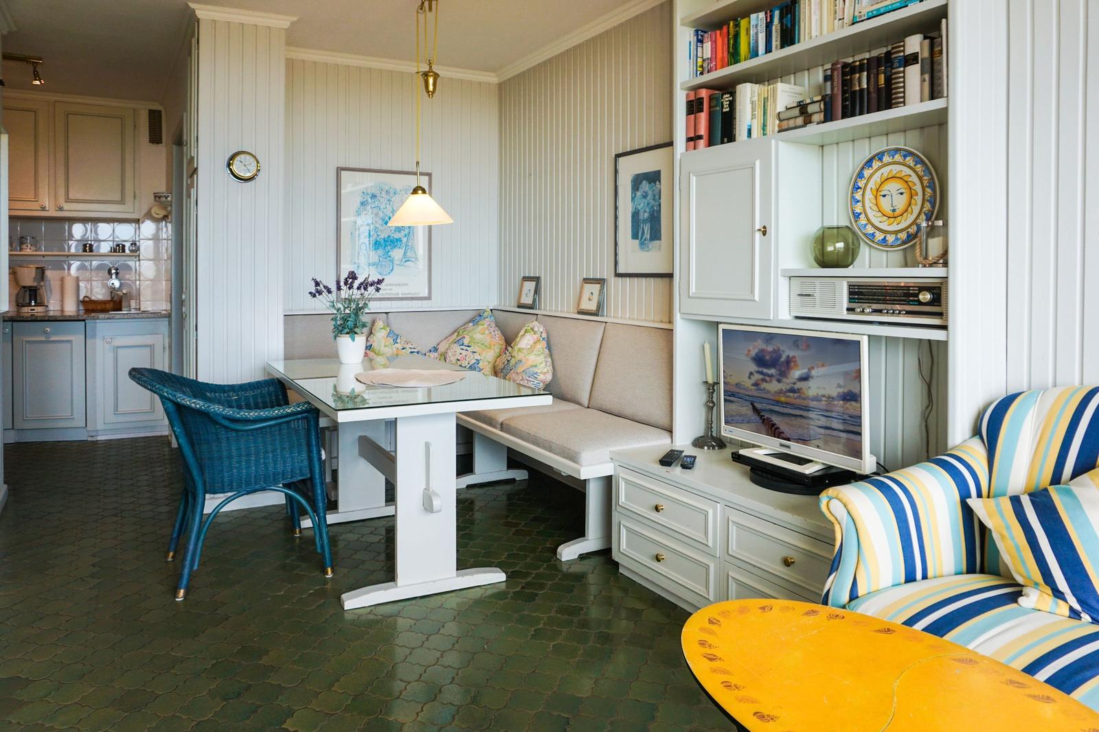 Dining area with bench, glass table, and blue chair. Living area with sofa and TV.