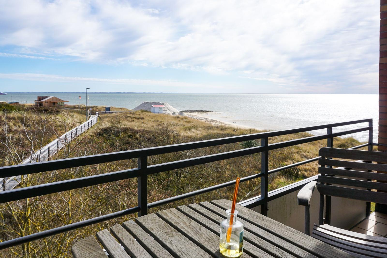 Terrace with table and chair offers view of beach and sea.