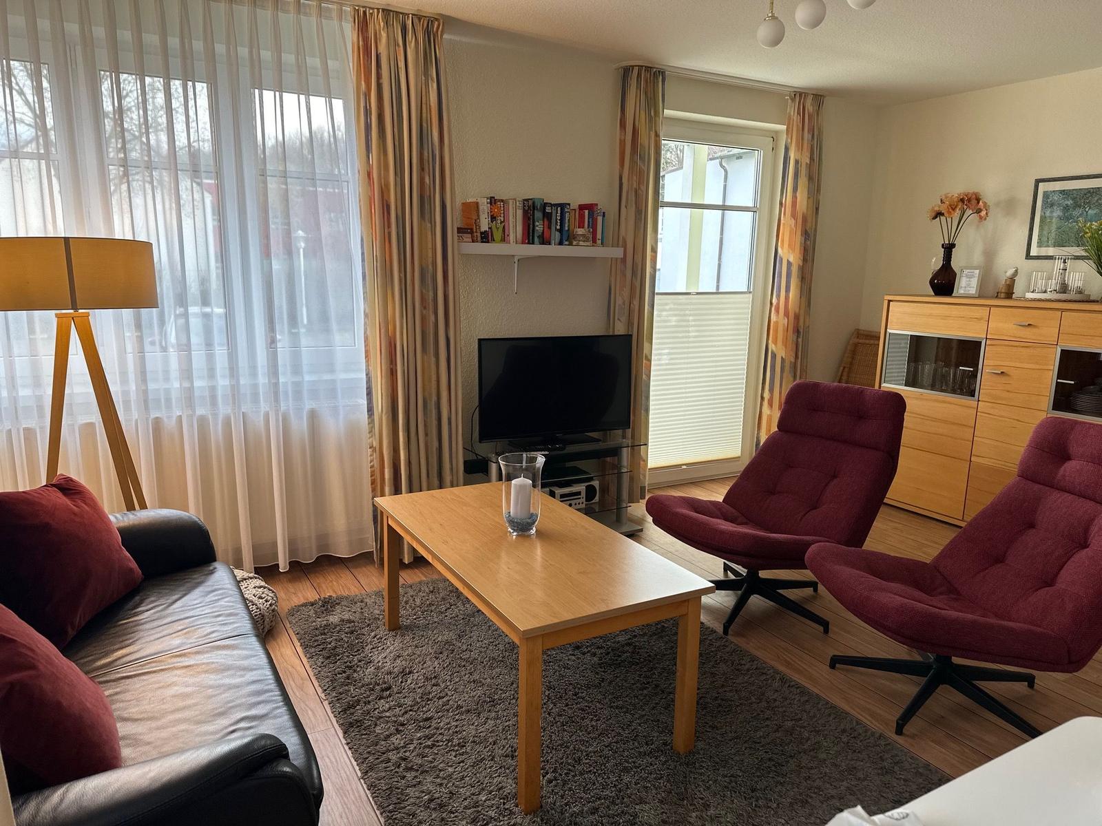 Wohnzimmer mit Sofa, zwei roten Sesseln, Couchtisch und Fernseher.