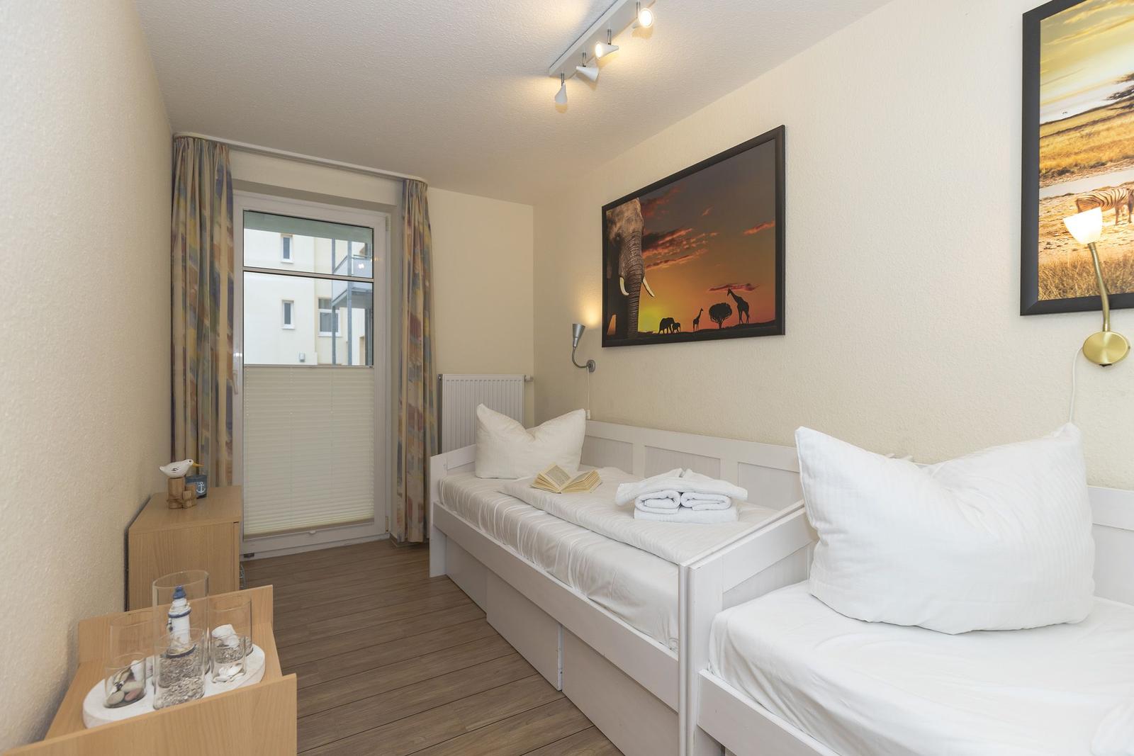 Zwei Betten mit weißen Laken, Wandbilder und Fenster mit Vorhängen.