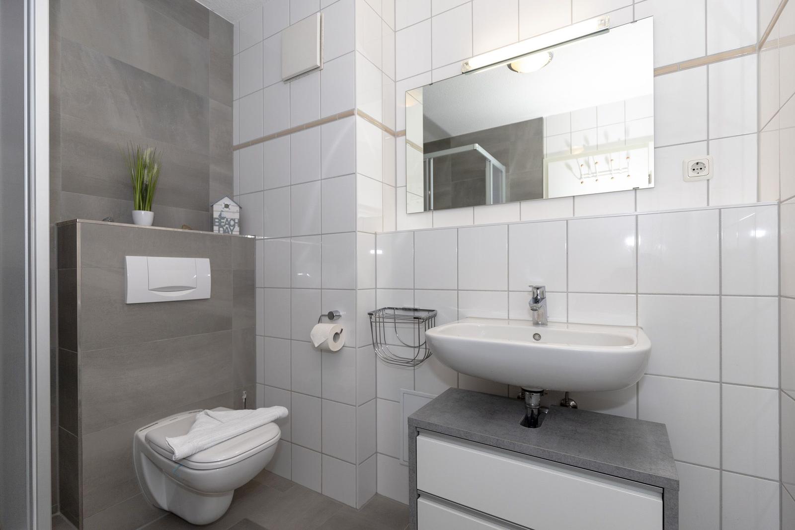 Badezimmer mit Toilette, Waschbecken und Spiegel. Fliesenwand und graue Arbeitsplatte.