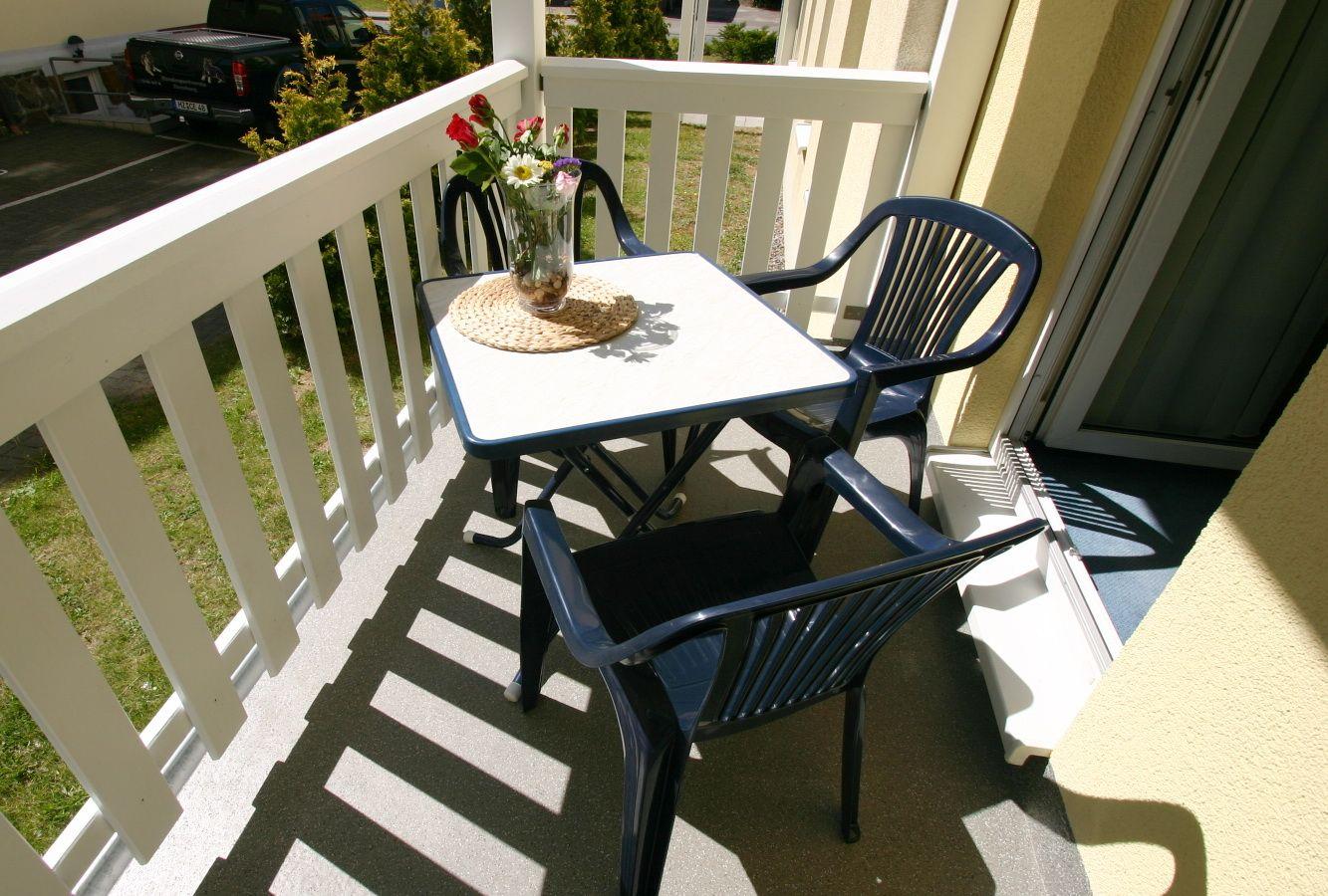 Terrasse mit Tisch und drei Stühlen, Blumen in Vase, weißer Geländer