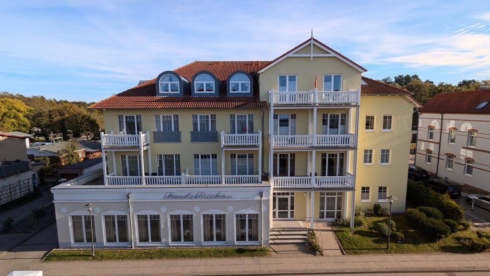 Ferienhaus mit Balkonen und Dachfenstern, hellgelb gestrichen, mit Eingangsbereich und Rasenfläche.