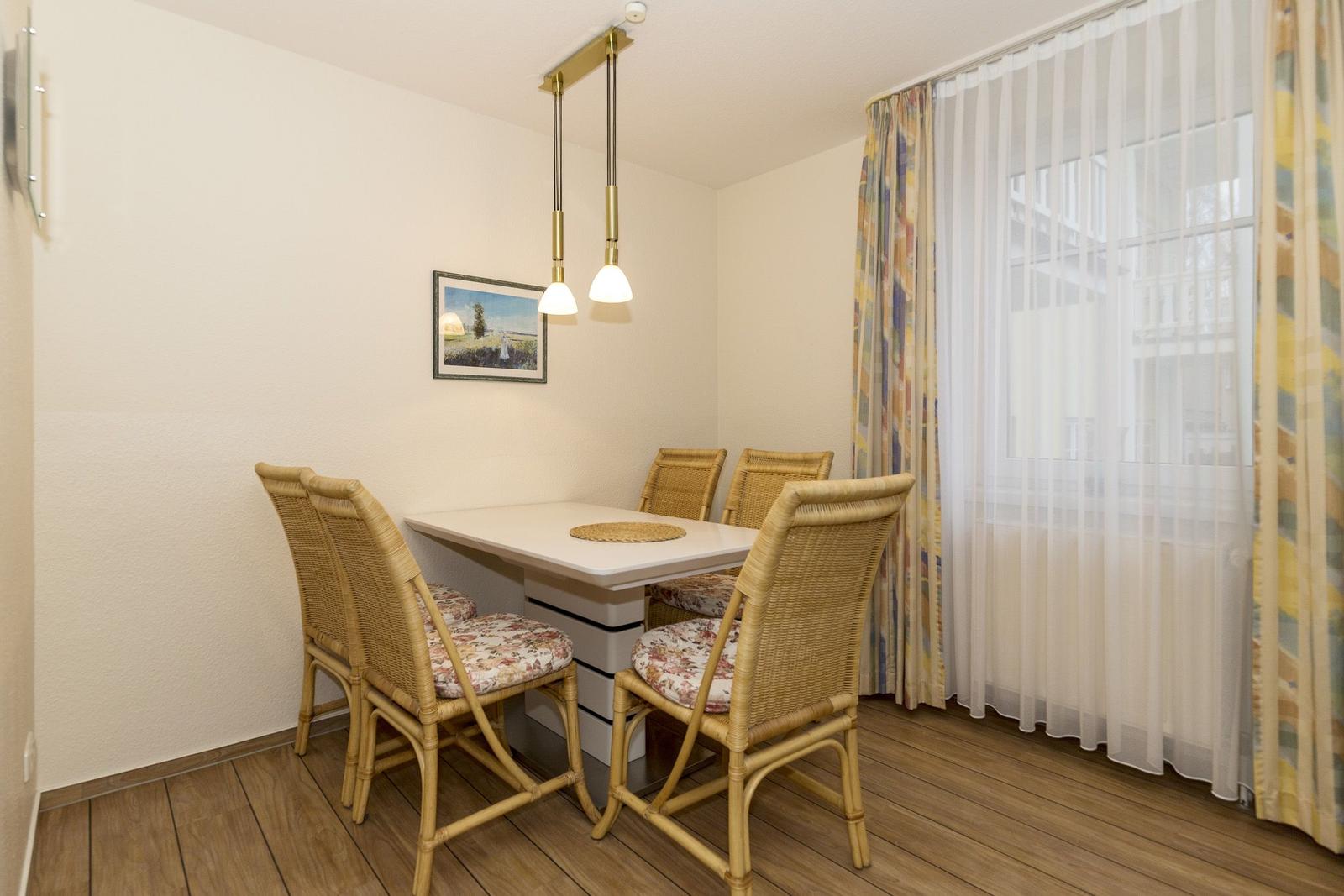 Essbereich mit Tisch und vier Stühlen, Fenster mit Vorhängen und Deckenleuchte.