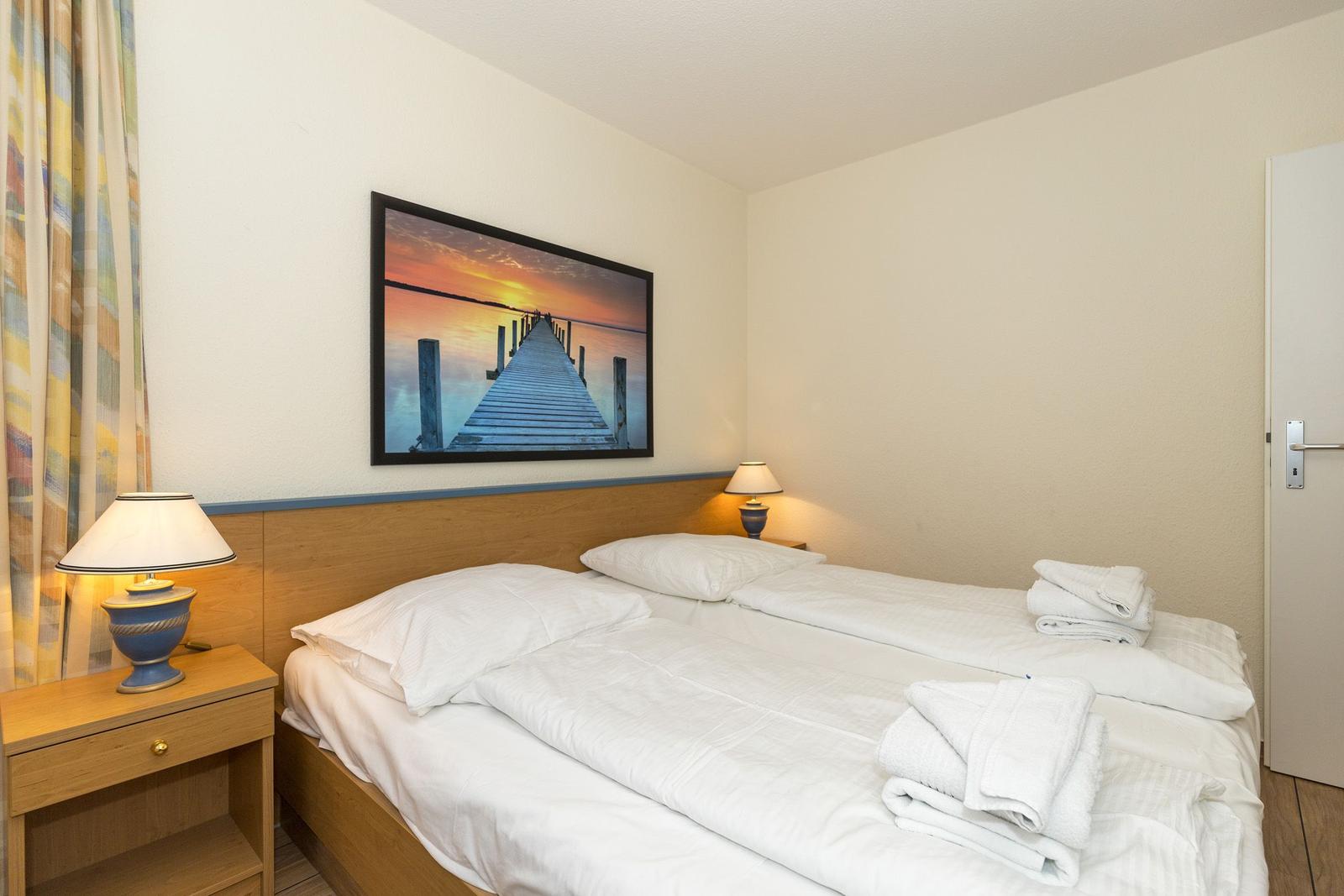 Zimmer mit Doppelbett, zwei Nachttischen und Wandbild eines Stegs.
