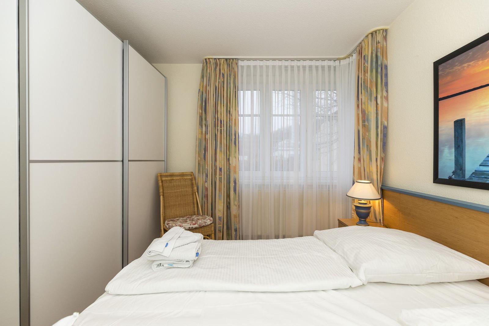 Schlafzimmer mit Bett, Gardinen, Nachttisch und Kleiderschrank.