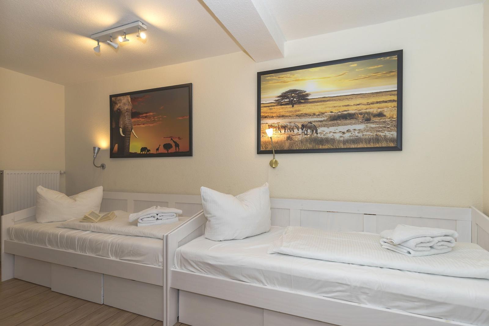 Zwei weiße Betten mit Kissen und Handtüchern an der Wand mit afrikanischen Bildern.