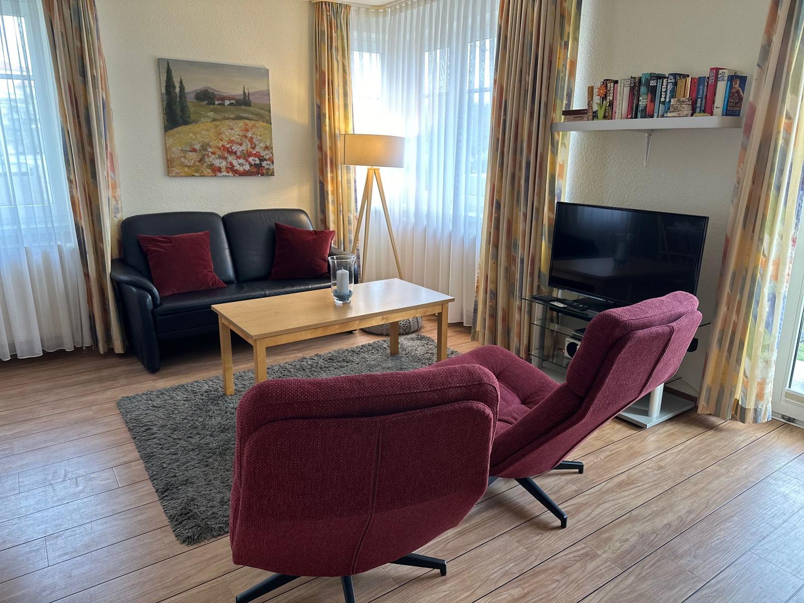 Wohnzimmer mit Sofa, zwei Sesseln, Couchtisch und Fernseher.