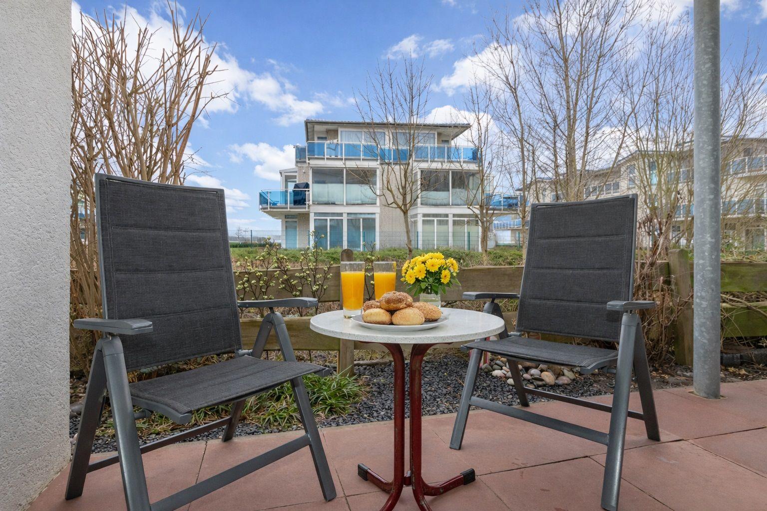 Terrace with two chairs and table. On the table are two glasses and a plate with pastries.