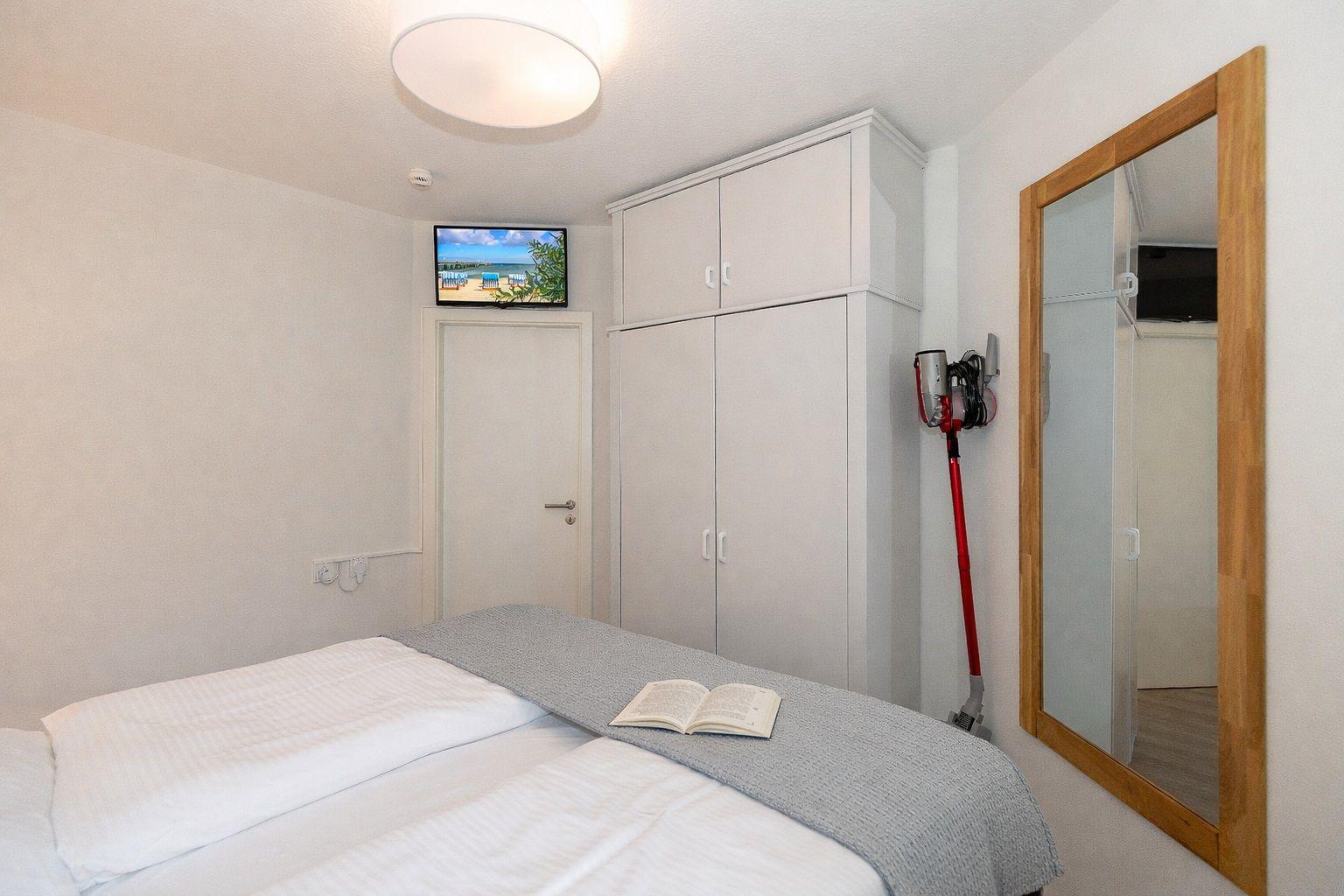 A bedroom with bed, wardrobe, mirror, and TV mounted on the wall.