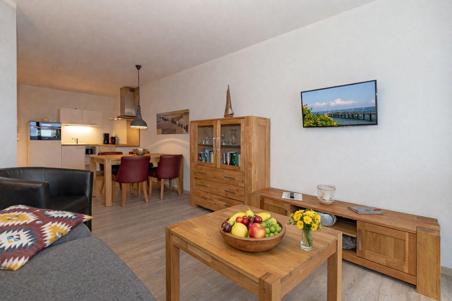 Living and dining area with wooden furniture, TV, and fruit bowl on table.