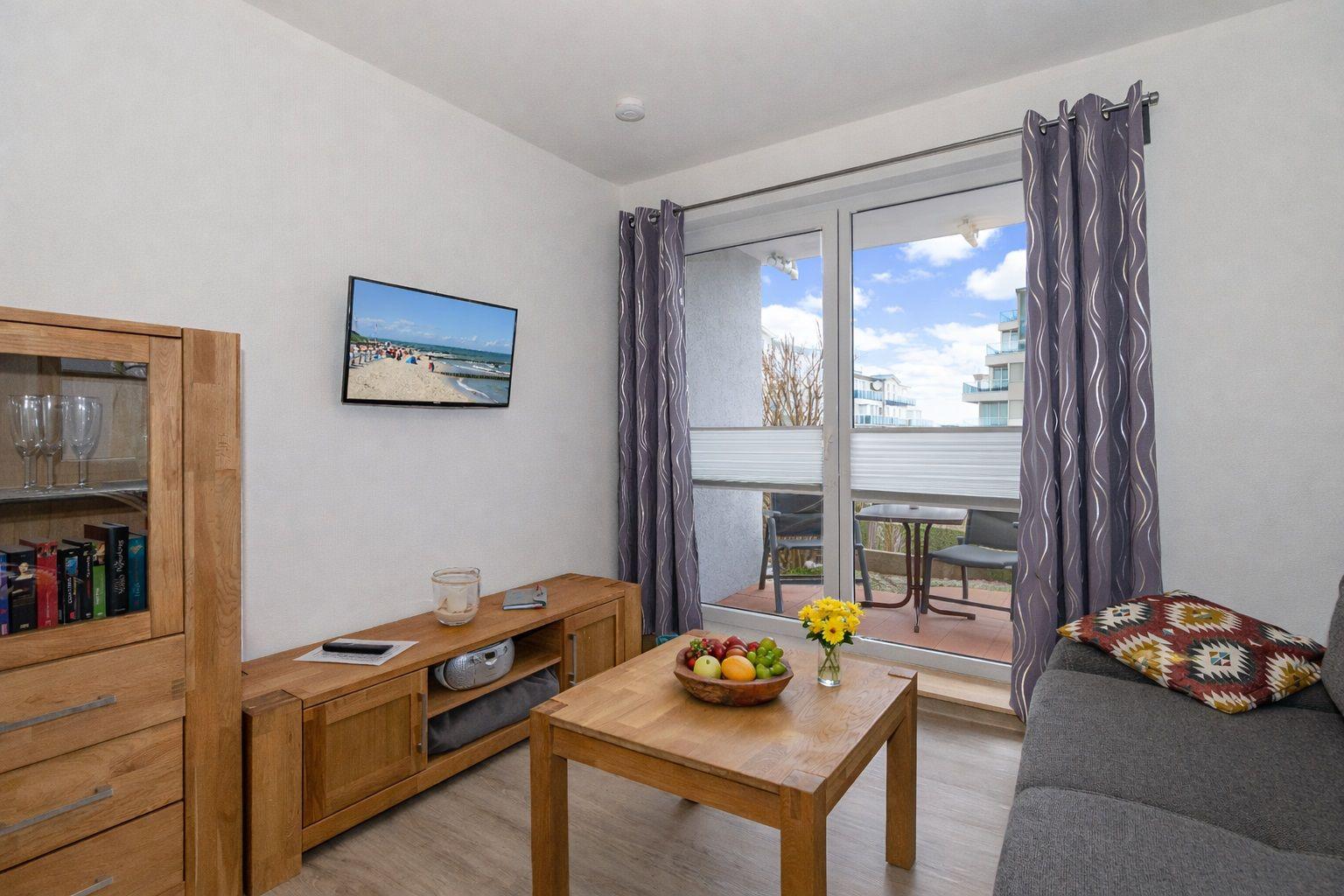 Living room with TV, wooden furniture, and balcony view of beach and sea.