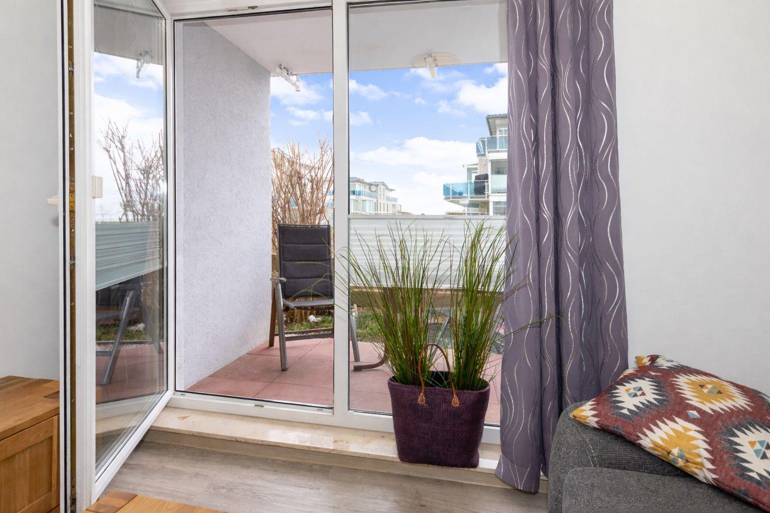 Sliding glass door leads to a terrace with chair and plant. Curtain and cushion are visible.