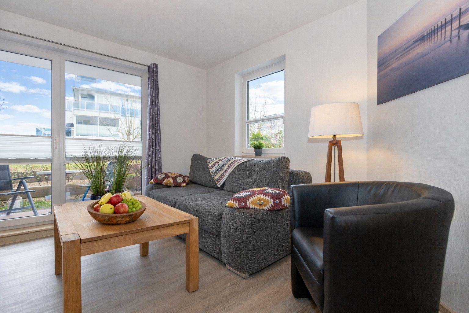Living room with sofa, armchair, table, and windows to terrace.