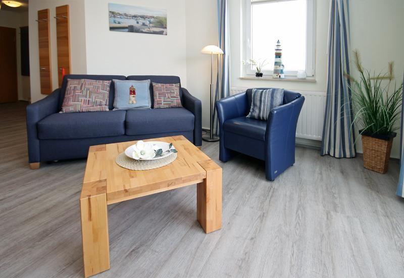 Living room with sofa, armchair, wooden table, and window. Blue upholstery and wooden floor.