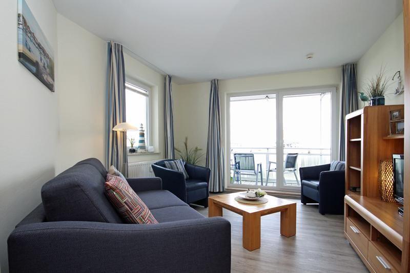 Living room with sofa, two chairs, table, and balcony with view.