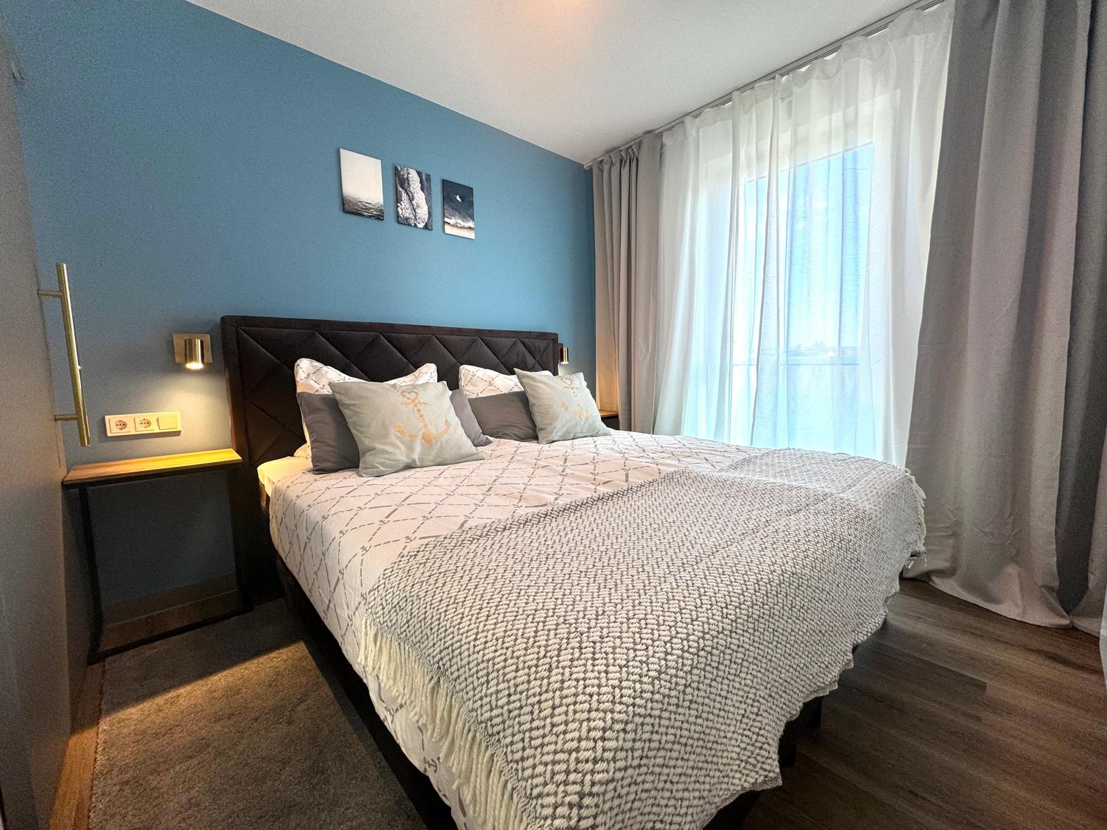 Schlafzimmer mit Bett, blauer Wand und Fenster mit Vorhängen.