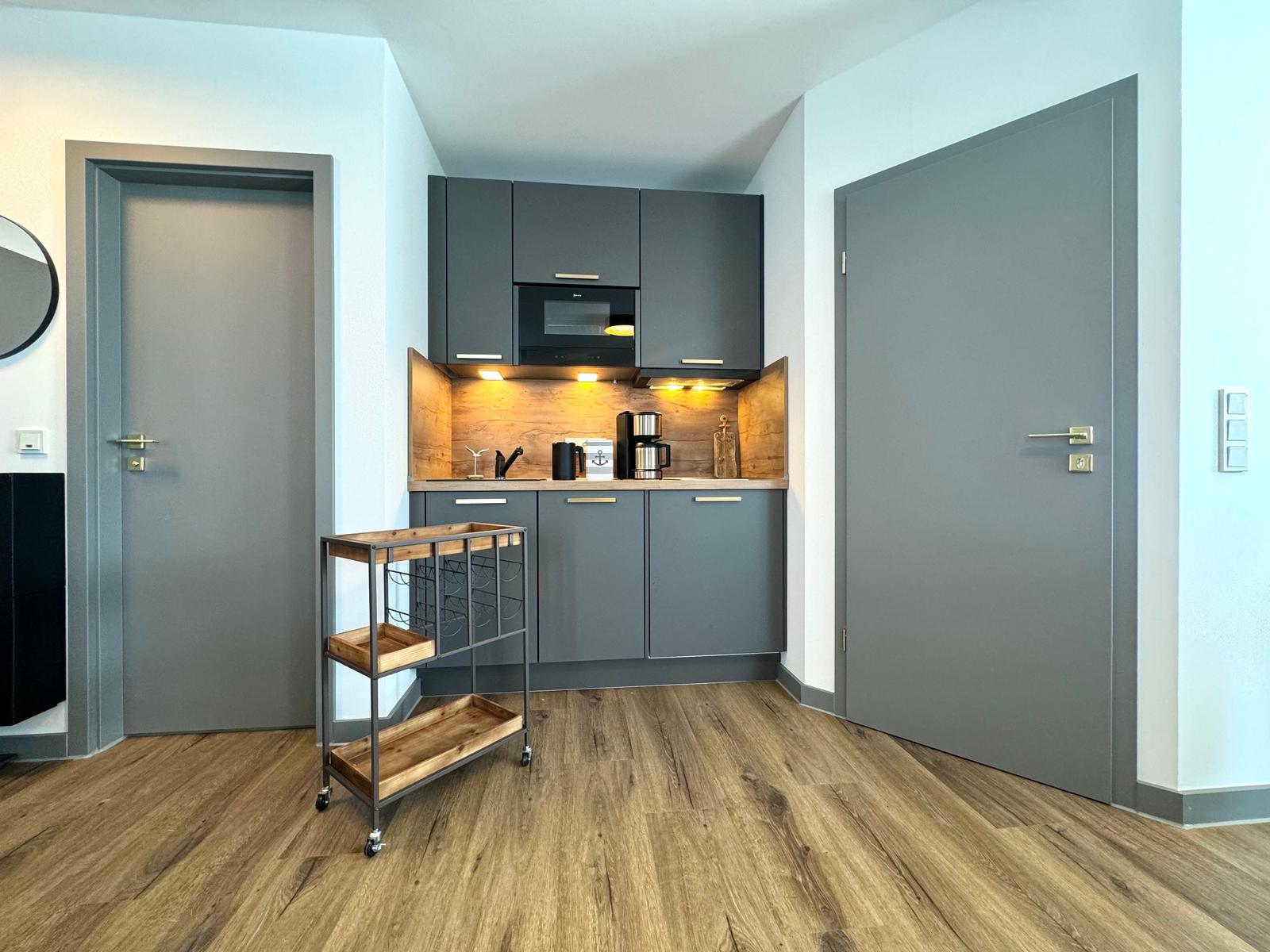Küche mit grauen Schränken, Holzoberfläche und Kühlschrank. Holzfußboden und zwei Türen.