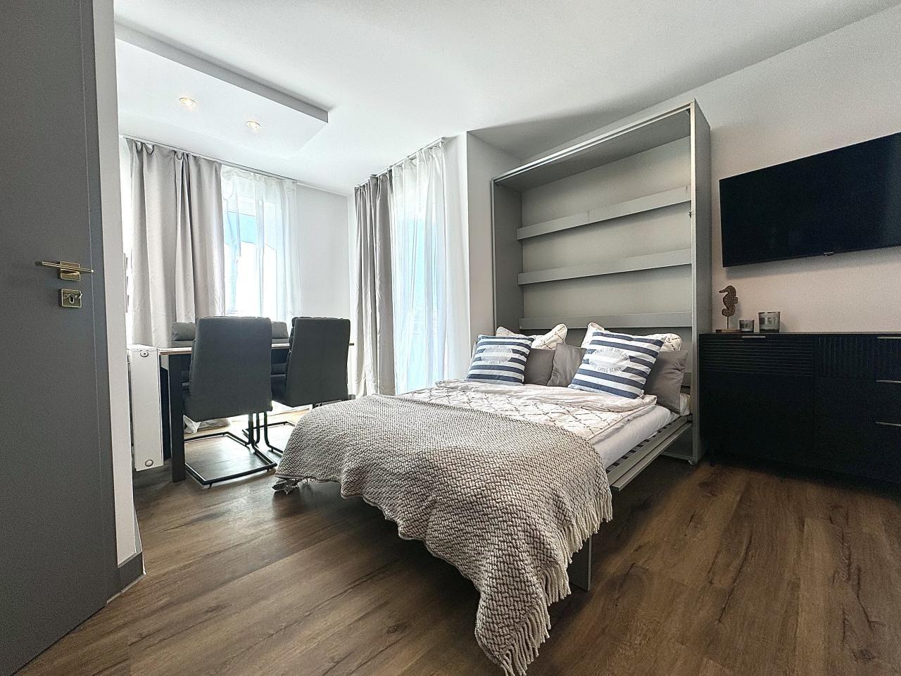 Schlafzimmer mit Bett, Fernseher und Essbereich mit Tisch und Stühlen.