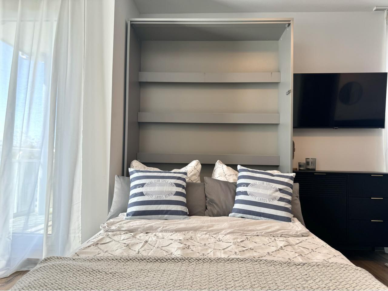 Schlafzimmer mit Bett, Kleiderschrank und Fernseher an der Wand.