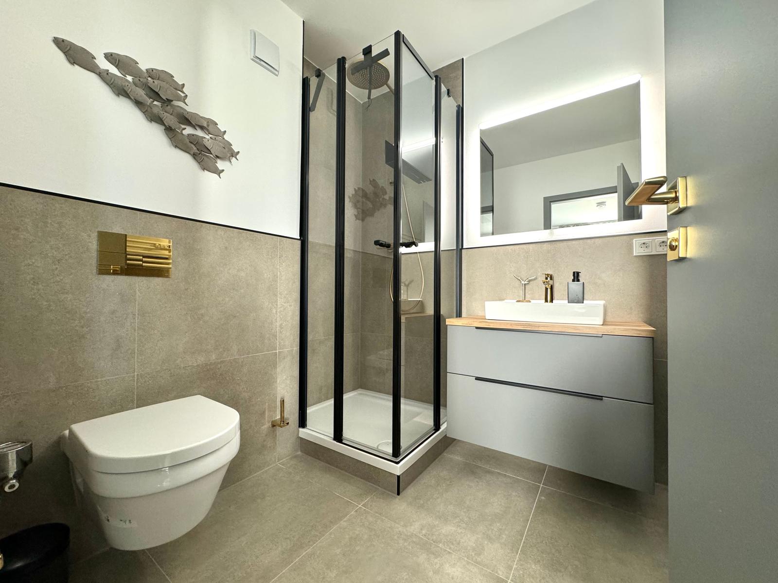 Badezimmer mit Dusche, Waschbecken und Toilette. Wanddekoration und goldene Akzente.