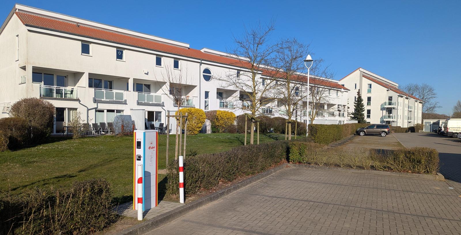 Wohnhaus mit Balkonen, Grünflächen und Parkplatz. Energieversorgung durch Ladesäule.