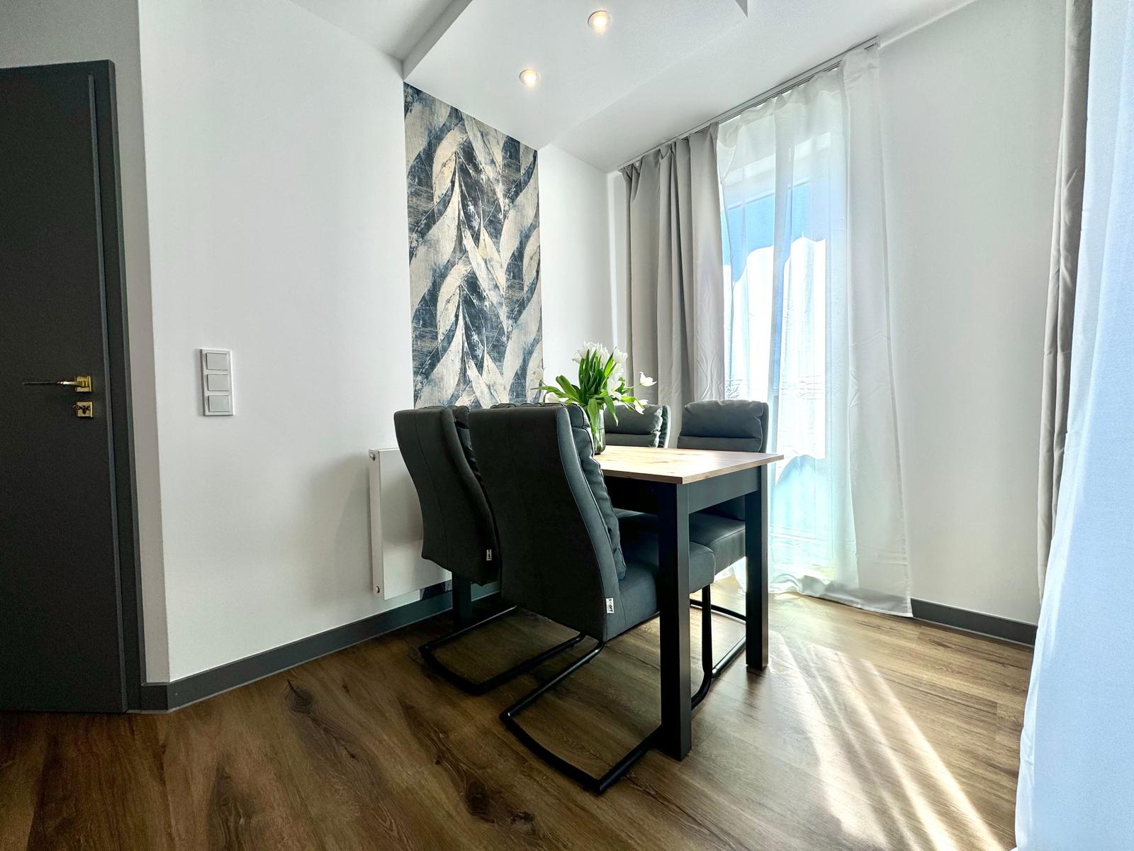 Essbereich mit Tisch, Stühlen und Fenster. Wandbild und Holzboden sichtbar.