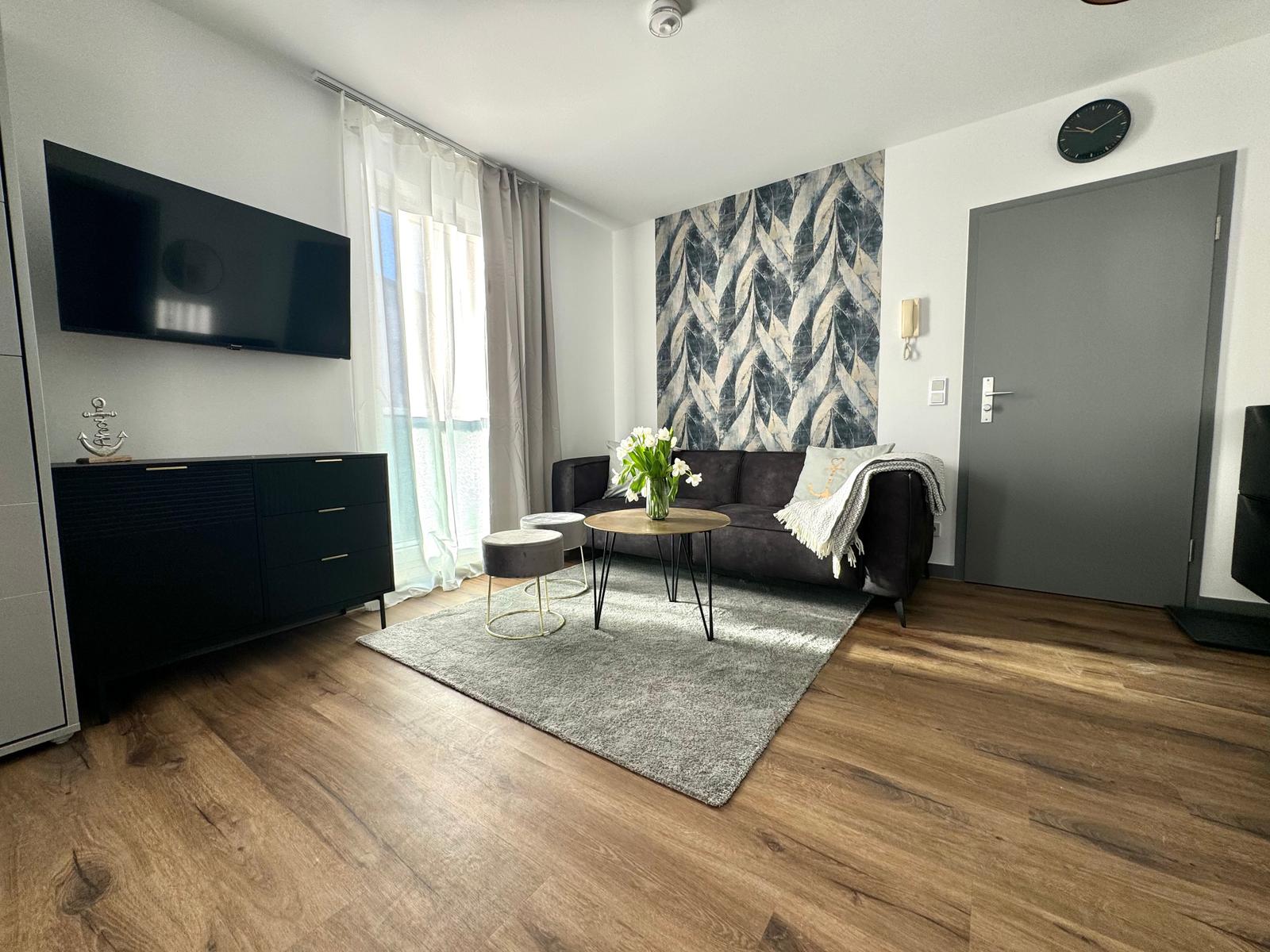 Wohnzimmer mit Sofa, TV, Tisch und Fenster. Wandbild und Holzboden.