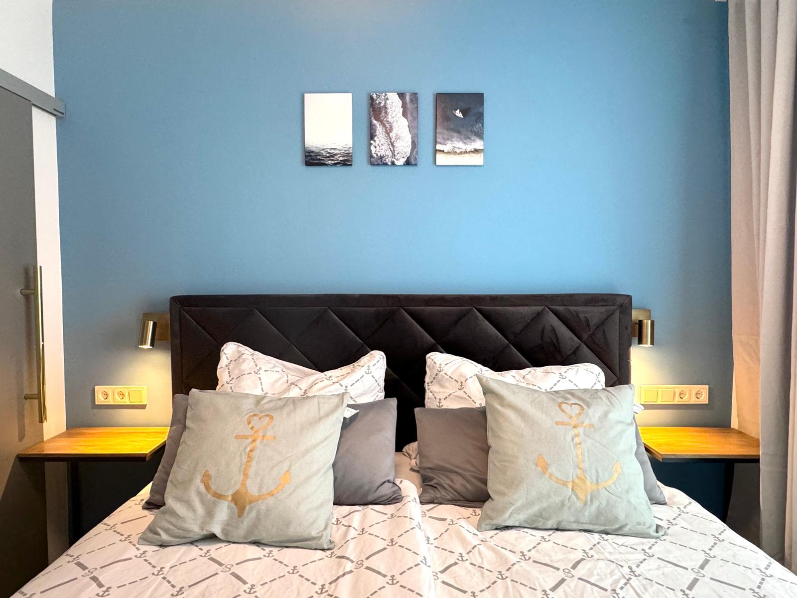 Schlafzimmer mit blauer Wand, dunklem Kopfteil und Kissen mit Anker-Motiv.