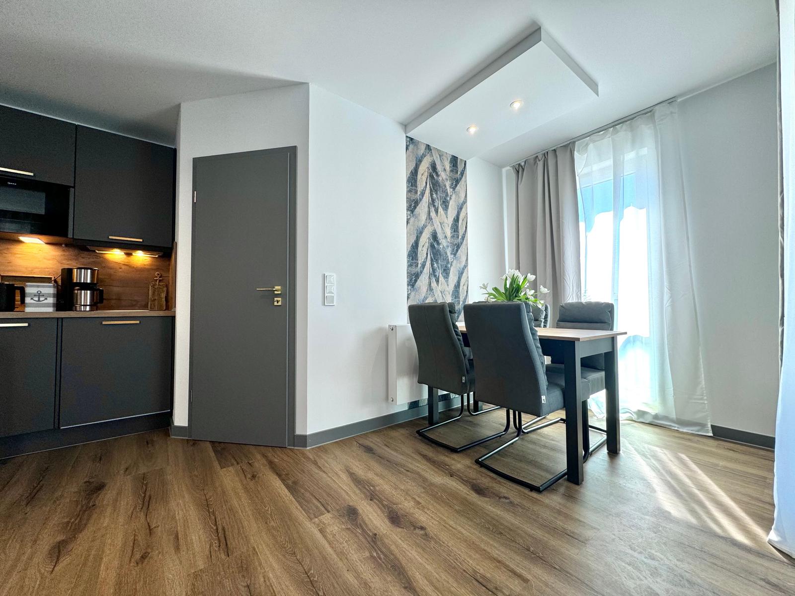 Küche mit Essbereich, Holzboden und Fenster mit Vorhängen.