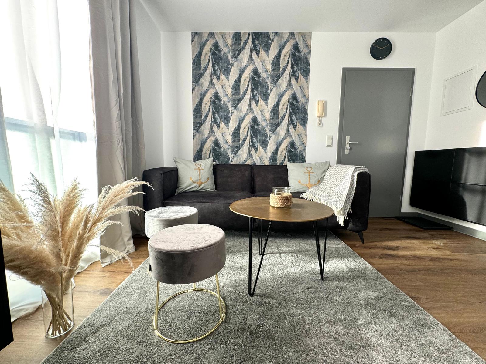 Wohnzimmer mit Sofa, Tisch und Sitzhocker. Wandbild und Fernseher sichtbar.