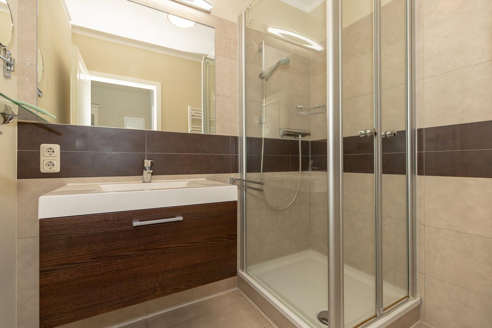 Badezimmer mit Dusche und Waschbecken mit dunkler Holzfront.