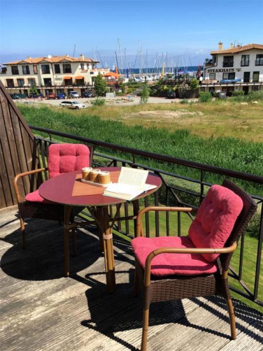 Terrasse mit Tisch und zwei Stühlen, Blick auf Hafen und Grünfläche.