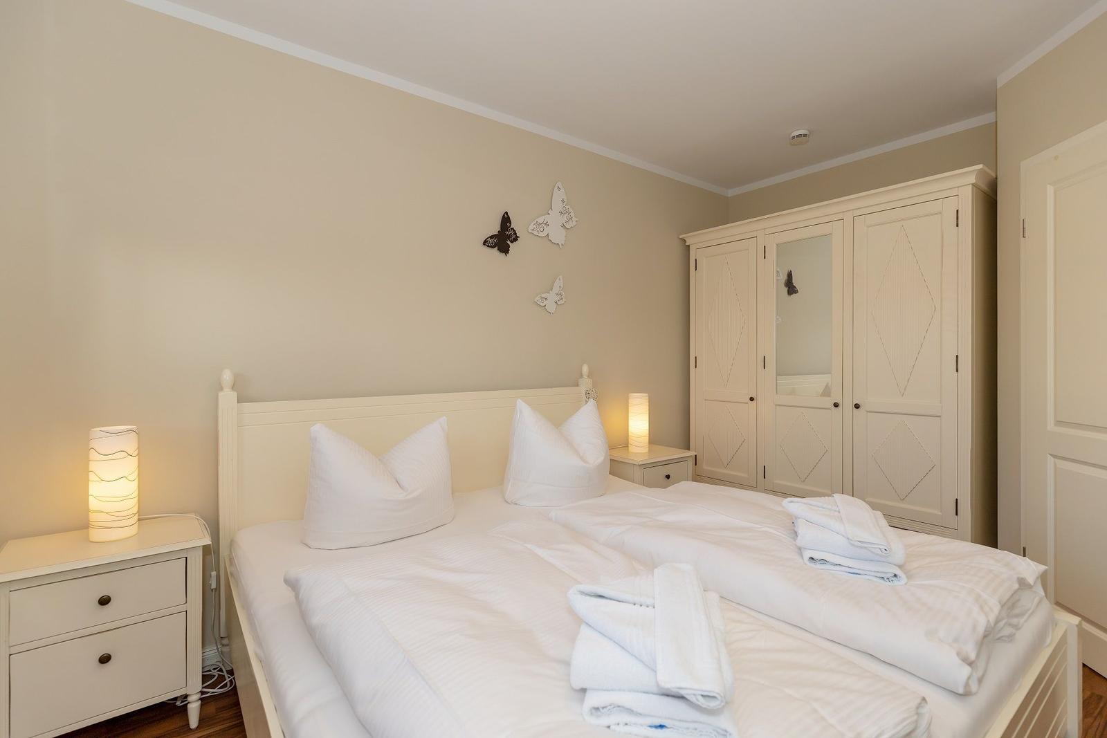 Schlafzimmer mit Doppelbett, Nachttischen und Kleiderschrank. Wände in Cremetönen.