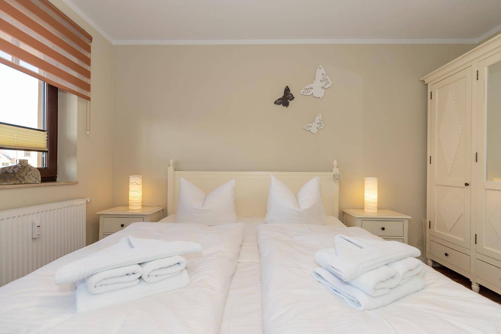 Zimmer mit Doppelbett, zwei Nachttischen, Schrank und Fenster mit Rollladen.