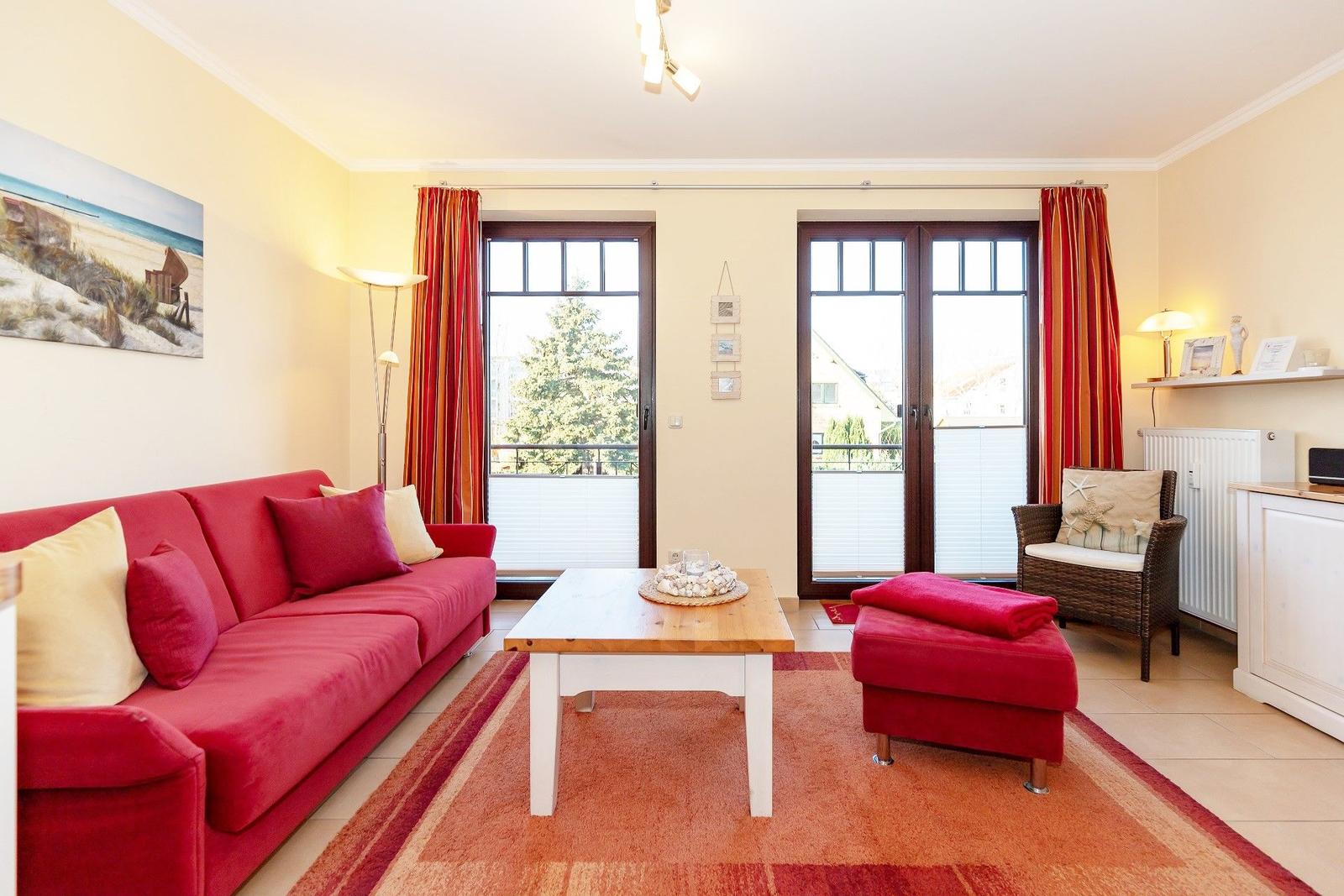 Ein Wohnzimmer mit rotem Sofa, Holztisch und Blick auf Balkon.