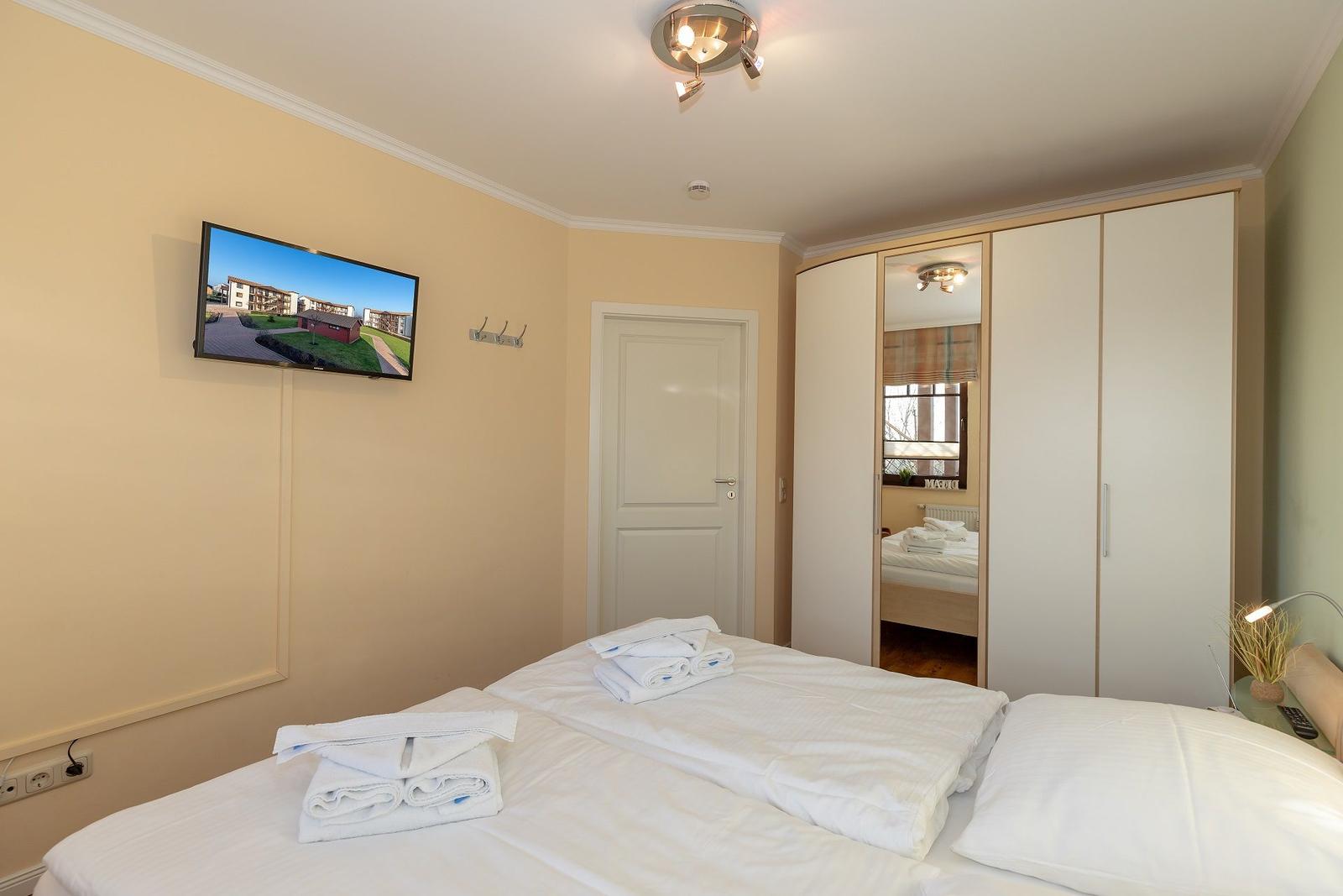 Schlafzimmer mit Doppelbett, Kleiderschrank und Wandfernseher.
