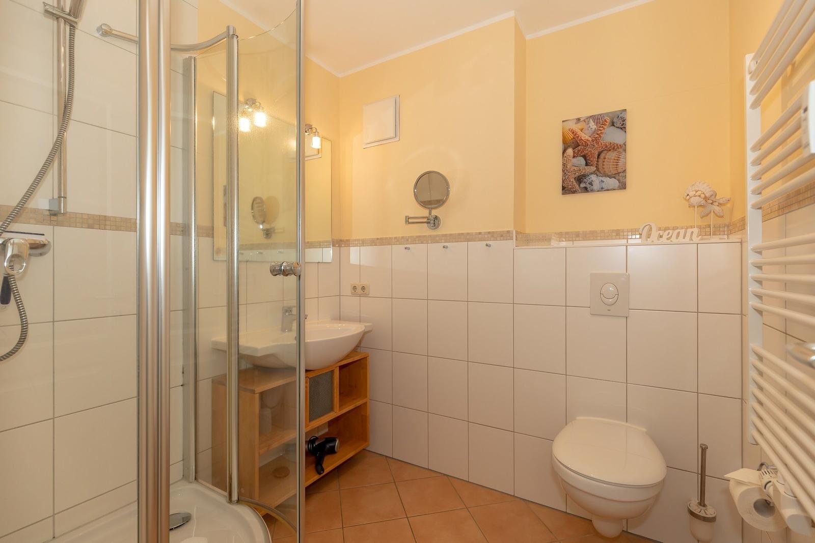 Badezimmer mit Dusche, Waschbecken und Toilette. Wandbild mit Meeresmotiv.