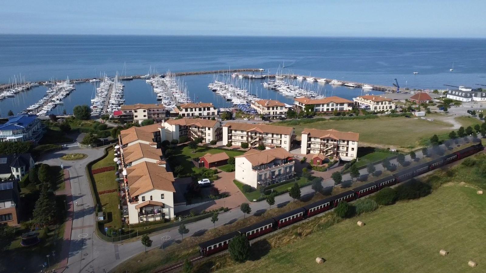 Häuser mit roten Dächern neben Hafen mit Booten und Eisenbahn
