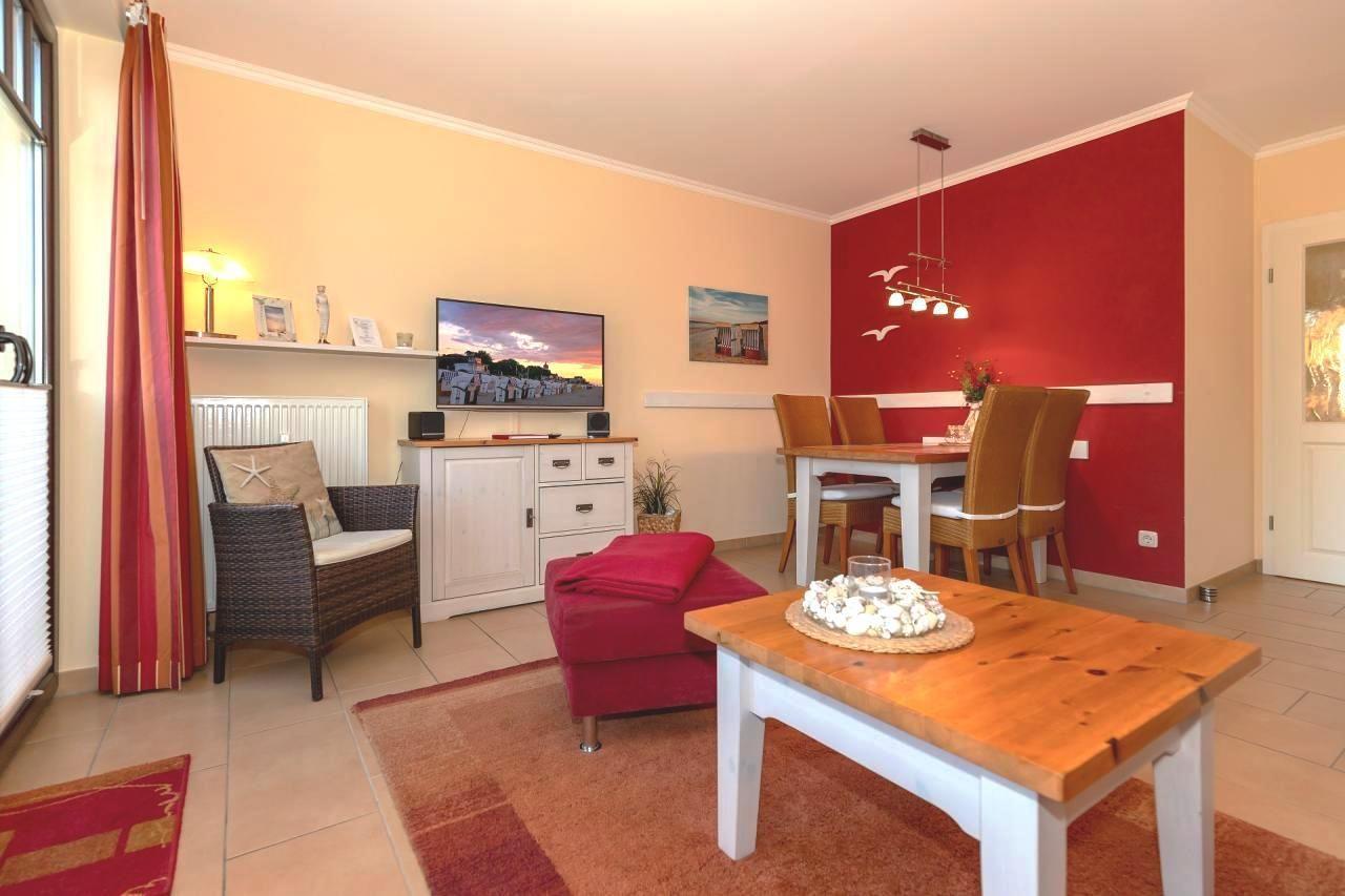 Wohn- und Essbereich mit roter Wand, TV, Esstisch und Sitzgelegenheiten.
