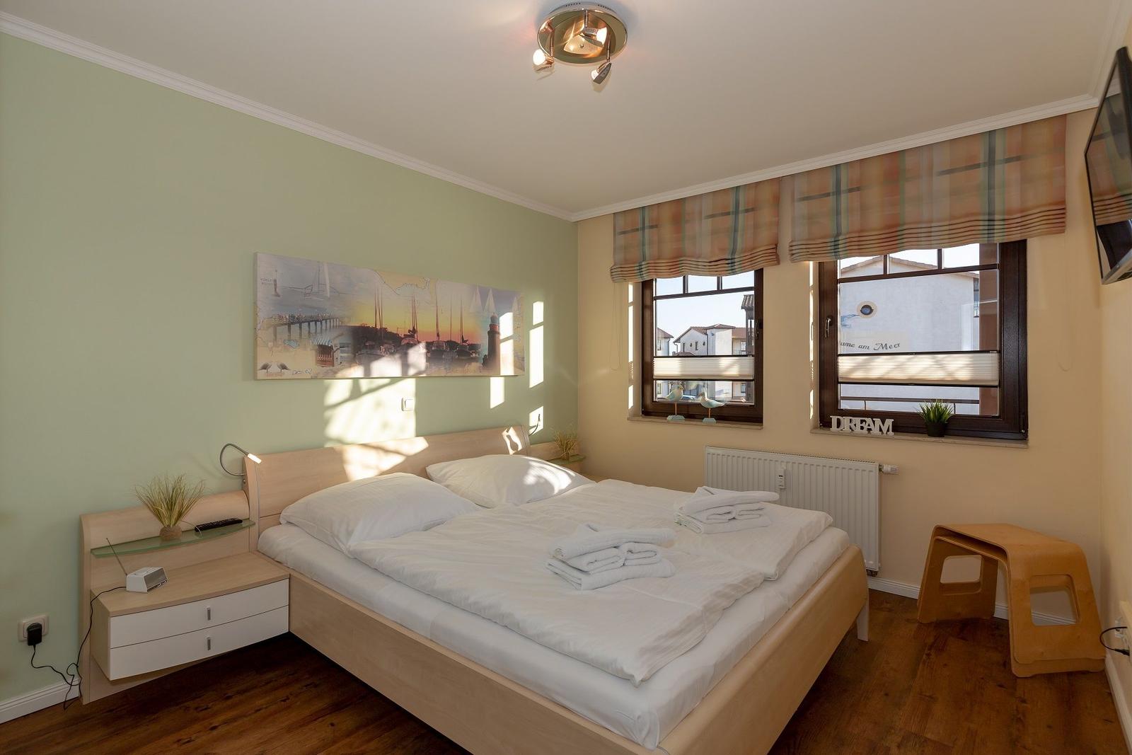 Schlafzimmer mit Doppelbett, Fenster und Nachttisch.