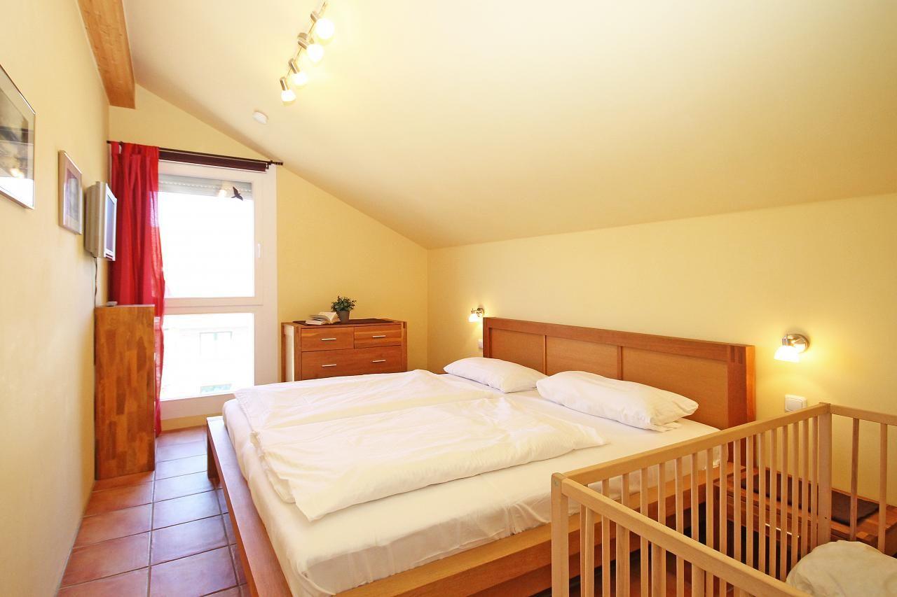 Schlafzimmer mit Doppelbett, Holzgeländer und Fenster mit roten Vorhängen.