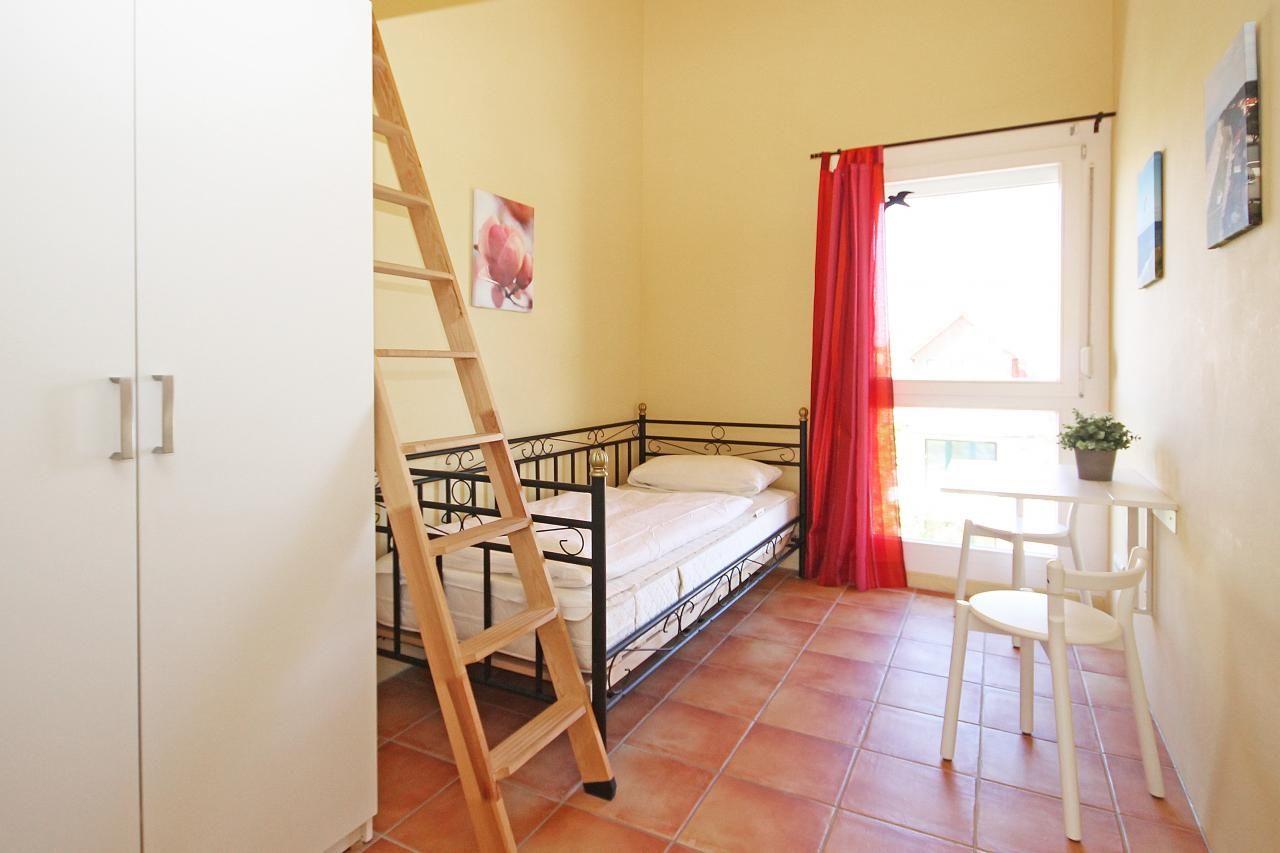 Schlafzimmer mit Doppelbett, Holztreppe, Fenster und Tisch mit Stühlen.
