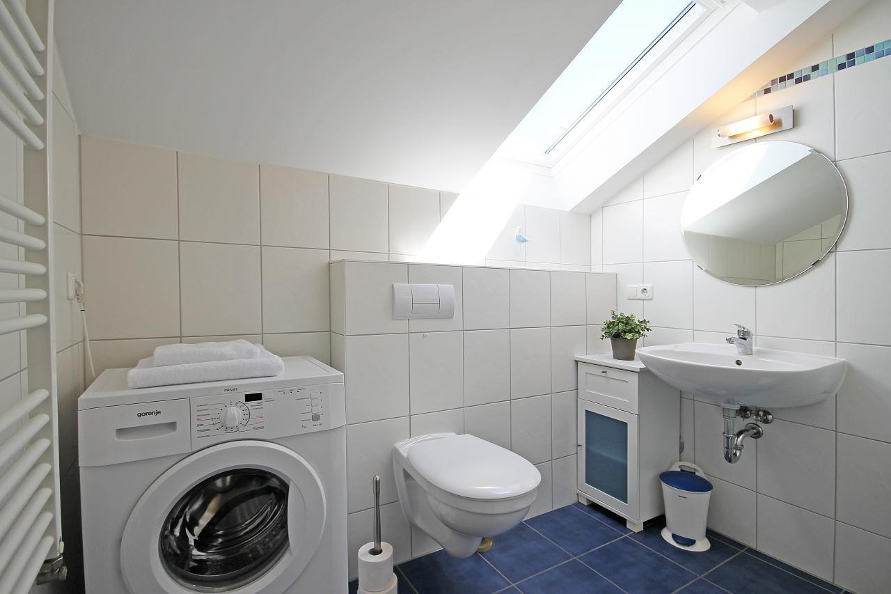 Badezimmer mit Waschmaschine, Toilette und Waschbecken unter Dachschräge.